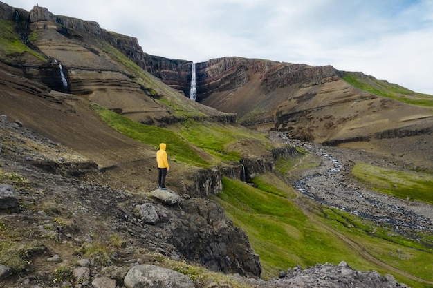 Aerial view a man in yellow coat enjoying Hengifoss Waterfall in Iceland