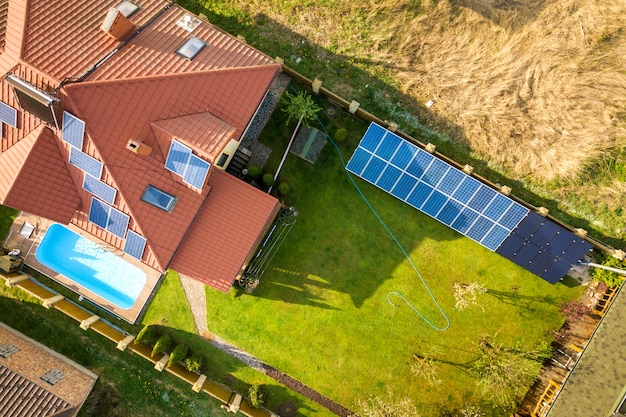 Aerial view of a private house with green grass covered yard, solar panels on roof, swimming pool and wind turbine generator.