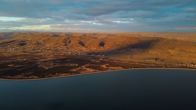 Aerial view of a river with yellow mountains and buildings under the cloudy sky