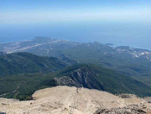 Aerial view of rocky mountainous coast with green trees and blue sea with white foaming waves