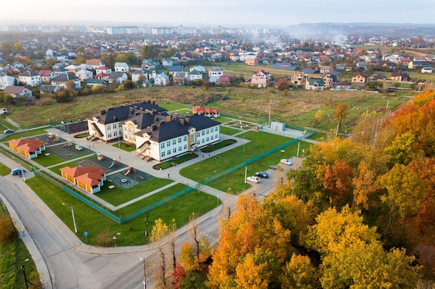 Aerial view of school college or kindergarten building with big yard among autumn trees on rural landscape background