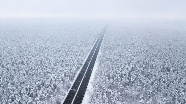 Aerial view of snow covered road in winter forest, truck passing by, motion blur