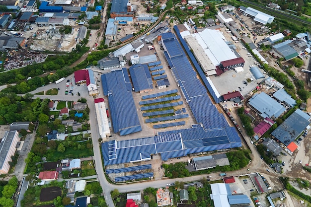 Aerial view of solar power plant with blue photovoltaic panels mounted on industrial building roof for producing green ecological electricity. Production of sustainable energy concept.