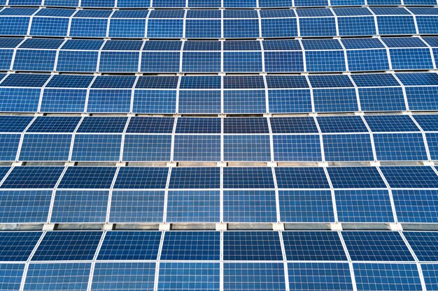 Aerial view of solar power plant with blue photovoltaic panels mounted on industrial building roof for producing green ecological electricity. Production of sustainable energy concept.