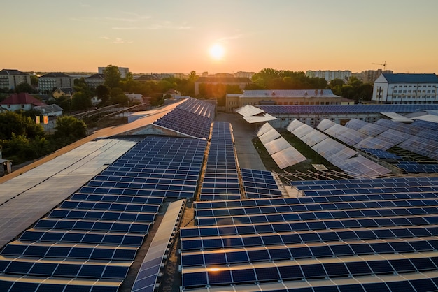 Aerial view of solar power plant with blue photovoltaic panels mounted on industrial building roof for producing green ecological electricity at sunset Production of sustainable energy concept