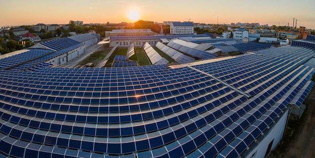 Aerial view of solar power plant with blue photovoltaic panels mounted on industrial building roof for producing green ecological electricity at sunset Production of sustainable energy concept