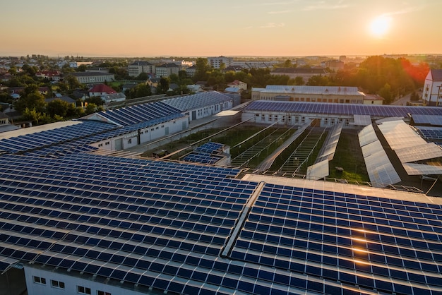 Aerial view of solar power plant with blue photovoltaic panels mounted on industrial building roof for producing green ecological electricity at sunset Production of sustainable energy concept