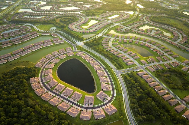 Aerial view of tightly packed homes in Florida closed living clubs with lake water in the middle Family houses as example of real estate development in american suburbs