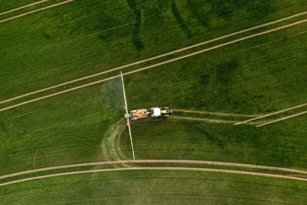 Aerial view of the tractor spraying the chemicals on the large green field