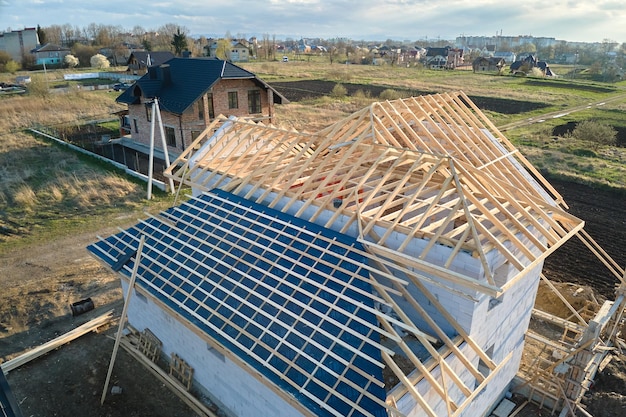 Aerial view of unfinished frame of private house with aerated lightweight concrete walls and wooden roof frame under construction.