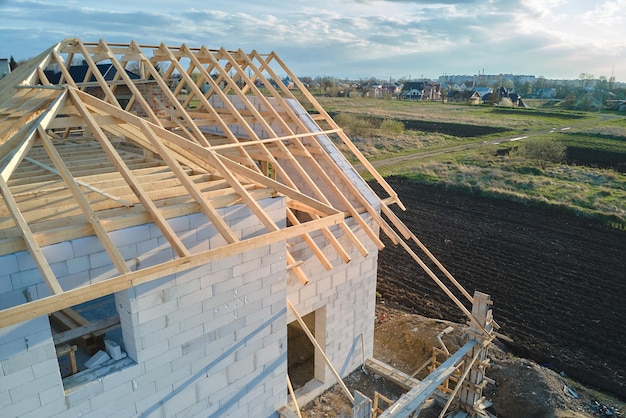 Aerial view of unfinished frame of private house with aerated lightweight concrete walls and wooden roof frame under construction.