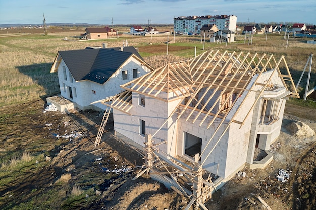 Aerial view of unfinished frame of private house with aerated lightweight concrete walls and wooden roof frame under construction.