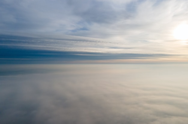 Aerial view of vibrant yellow sunrise over white dense clouds with blue sky overhead.