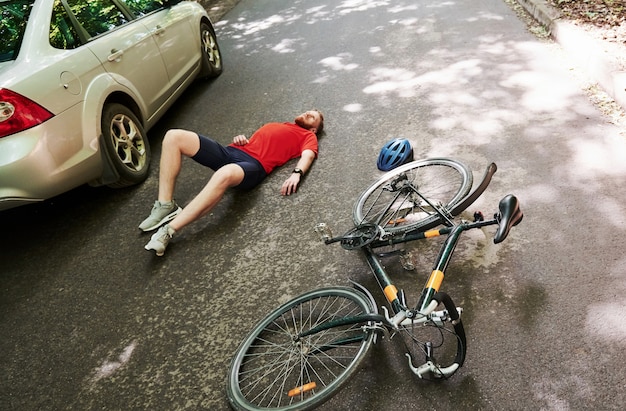 Aerial view. Victim on the asphalt. Bicycle and silver colored car accident on the road at forest at daytime