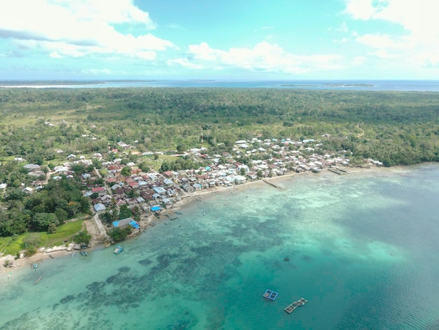 Aerial view of village near beautiful beach with small island in the background in Maluku, Indonesia