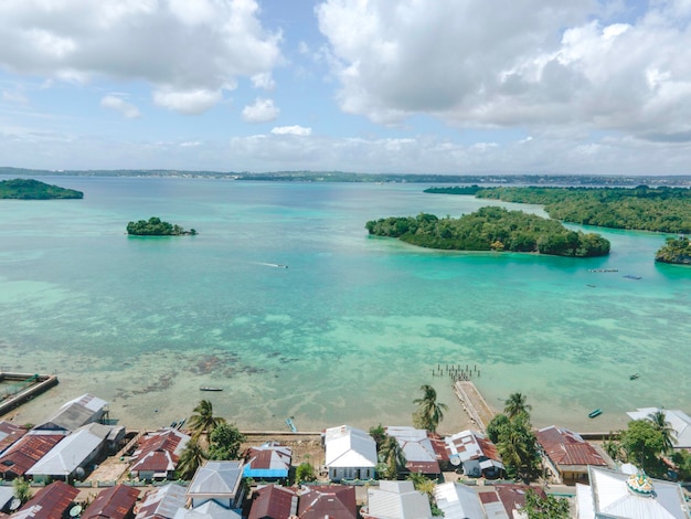 Aerial view of village near beautiful beach with small island in the background in Maluku, Indonesia