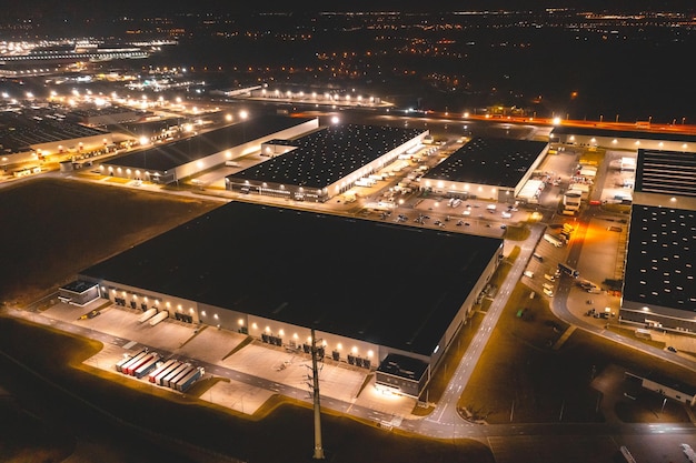 Aerial view of a warehouse of goods at night Many warehouses and trucks with trailers are in the parking lot waiting to be loaded for further distribution of goods around the country