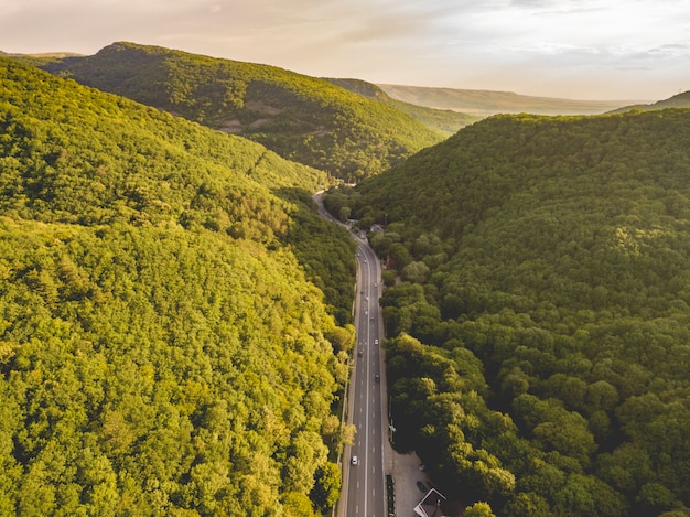 Aerial view of wide highway between the mountains covered with green woods