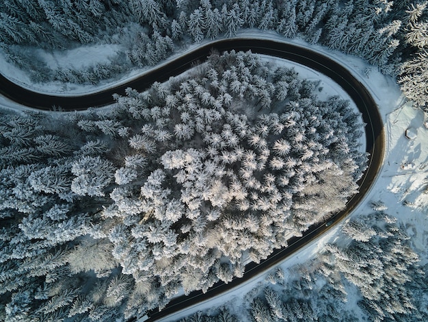 Aerial view of winter landscape with snow covered mountain hills and winding forest road in morning.