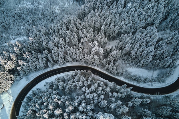 Aerial view of winter landscape with snow covered mountain hills and winding forest road in morning.