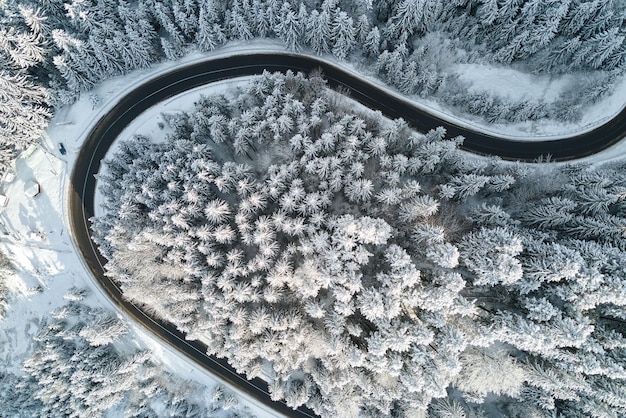 Aerial view of winter landscape with snow covered mountain woods and winding forest slippery road.