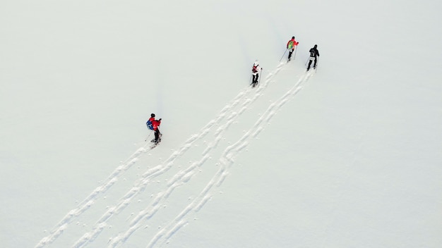 Aerial of winter snowshoeing across valley on sunset. Breathtaking natural landscape. Active group people in winter clothes snowshoeing on snowy lake. Travelers snowshoe explore locality