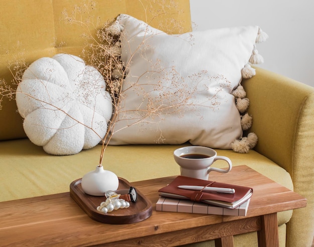 Photo the aesthetic appearance of the living room is a sofa with decorative pillows a cup of coffee and notebooks on a wooden bench