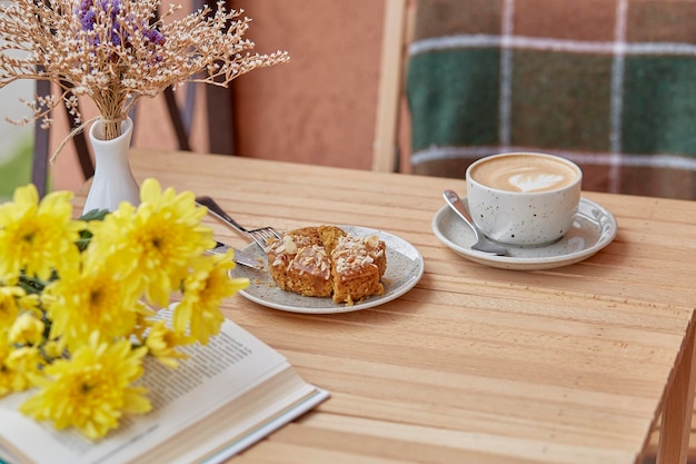 Aesthetic autumn lunch coffee time for yourself book and dessert Cutting doughnut with cappuccino among chrysanthemum Atmospheric lunch guilty pleasure