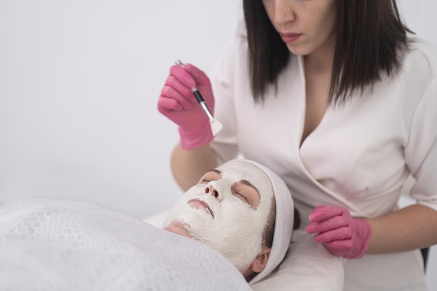 Aesthetic beautician applying face masks brush and perform facial treatments for middle age woman