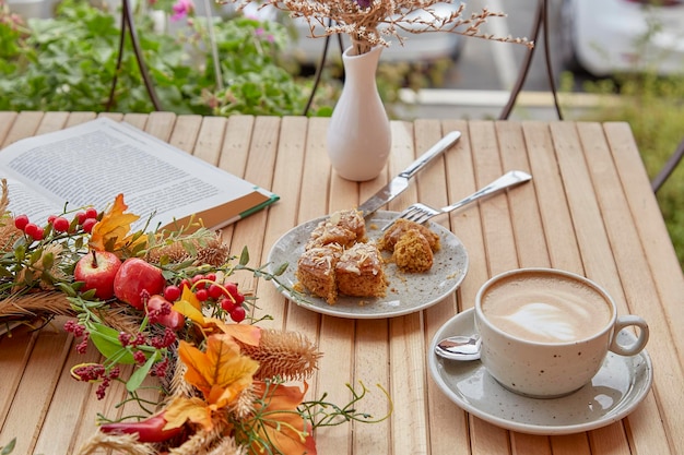 Aesthetic coffee time outside with a book cutting doughnut and cappuccino among fall decorations on wooden table Atmospheric coffee time