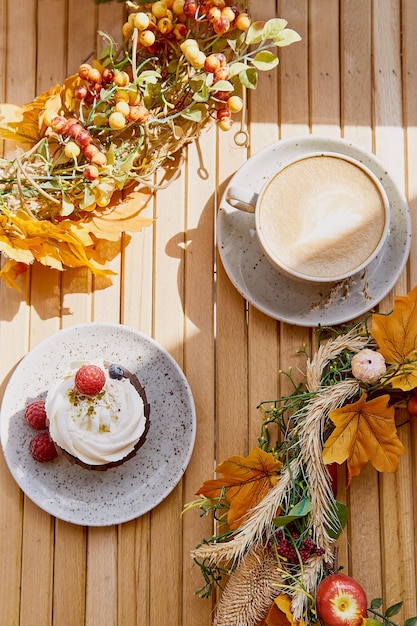 Aesthetic french berries cupcake and cup of cappuccino among autumn atmospheric decoration Cozy breakfast outside with trendy shadows