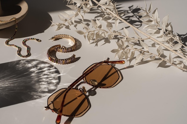 Aesthetic luxury fashion boutique branding composition Elegant bohemian glamour female jewelry and accessories with sun light shadows Sunglasses earrings bracelet plant