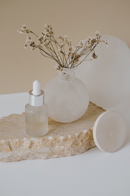 Photo aesthetic minimalist beauty care therapy concept. organic serum oil cosmetics bottle on stone with flowers against neutral beige