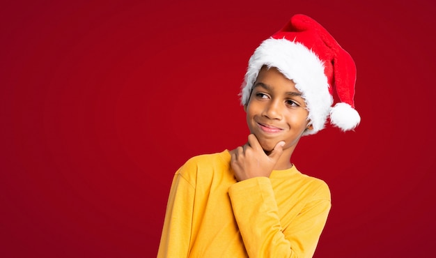 African American boy with christmas hat looking side over red background