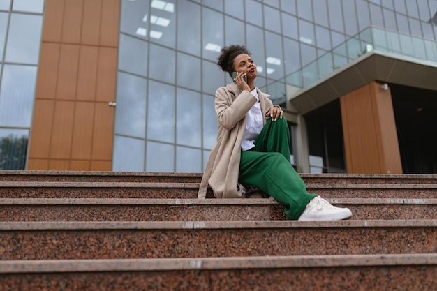 African american business woman talking on a mobile phone while sitting on the steps in front of an