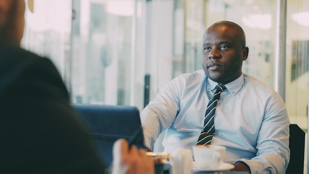 African American businessman explaining his startup details to investor in formal wear in glassy cafe during lunch time