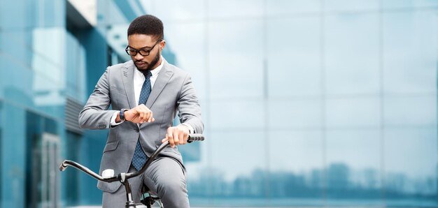 African american businessman in a suit is on a bicycle looking at his watch in a city setting the