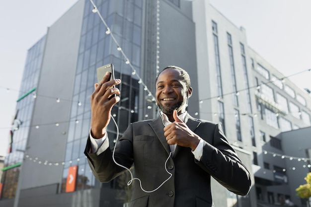 An african american businessman in a suit is standing outside an office center wearing headphones