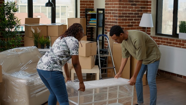 African american couple carrying furniture to decorate new home, using storage boxes to move in rented apartment flat. Moving in together and starting family in household property.