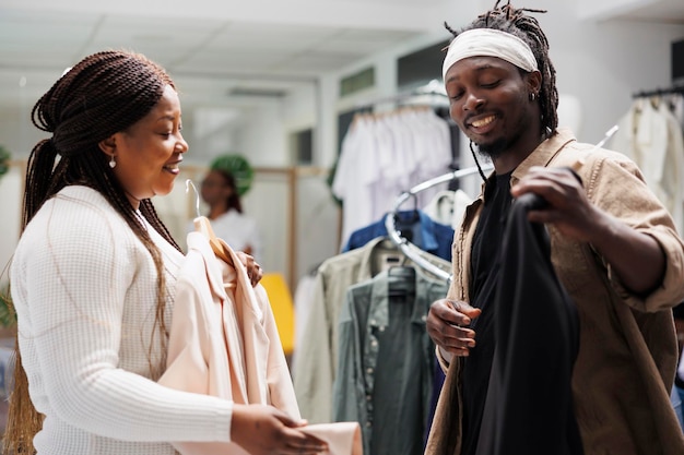 African american couple choosing formal jacket for special occasion in clothing store. Smiling young man showing modern blazer to woman and asking to try on in shopping mall