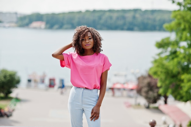 African american curlywoman posed at street of city wear on pink blouse and blue pants