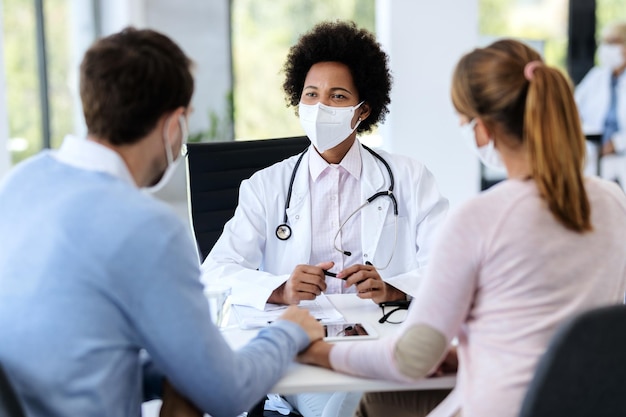 African American doctor wearing protective face mask during an appointment with a couple at clinic