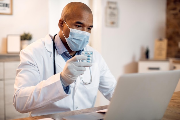 African American doctor with face mask advising a patient about the medicine via video call form his office