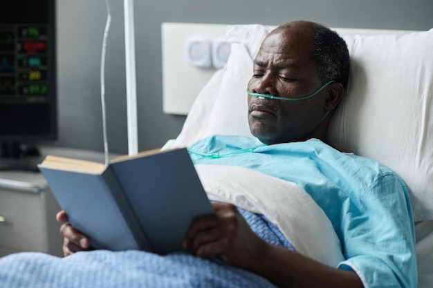 African american elderly patient reading book while lying in ward during his rehabilitation