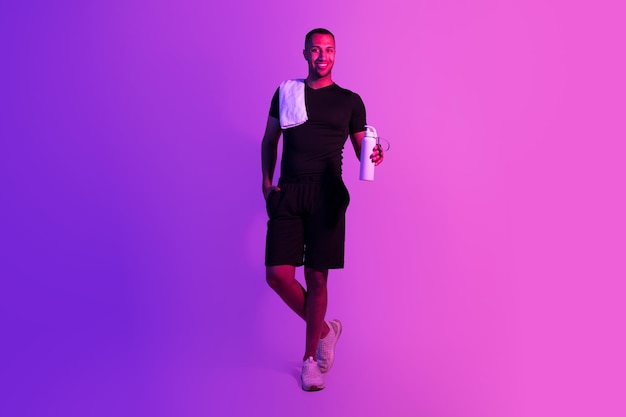 African american fitness guy holding water on purple studio background