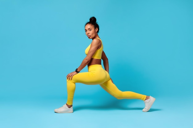 African american fitness lady stretching legs lunging forward blue background