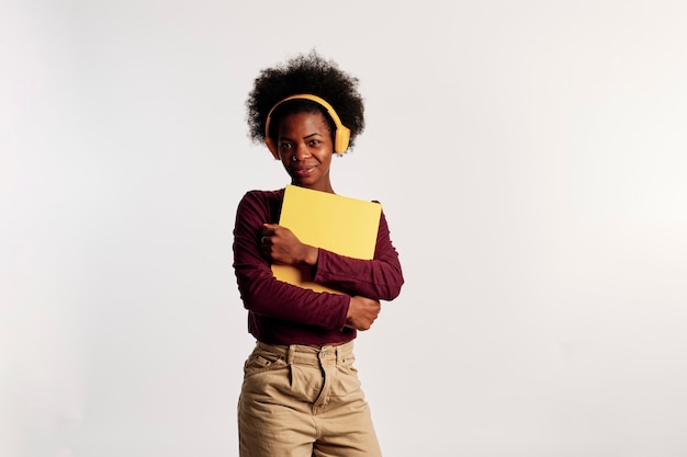 African American girl in brown sweater poses with her yellow folder while listening to music.