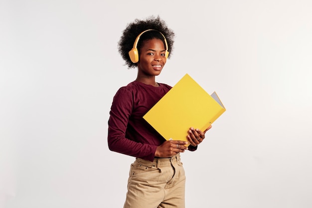 African American girl in brown sweater poses with her yellow folder while listening to music.