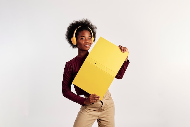 African American girl in brown sweater poses with her yellow folder while listening to music.