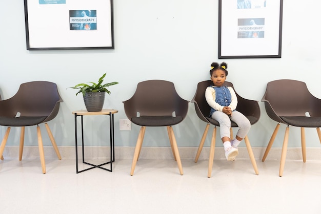 Photo african american girl patient sitting in waiting room at hospital, copy space. hospital, childhood, medicine and healthcare, unaltered.